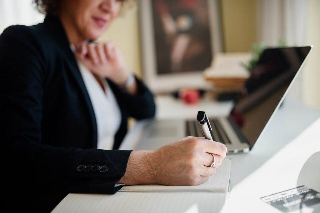 A Business Professional Is Seated At A Sleek Desk, Actively Taking Not — Business | RESIMLAND
