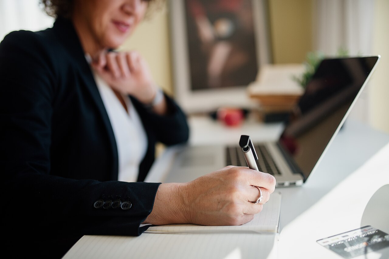 A Business Professional Is Seated At A Sleek Desk, Actively Taking Not — Business | RESIMLAND